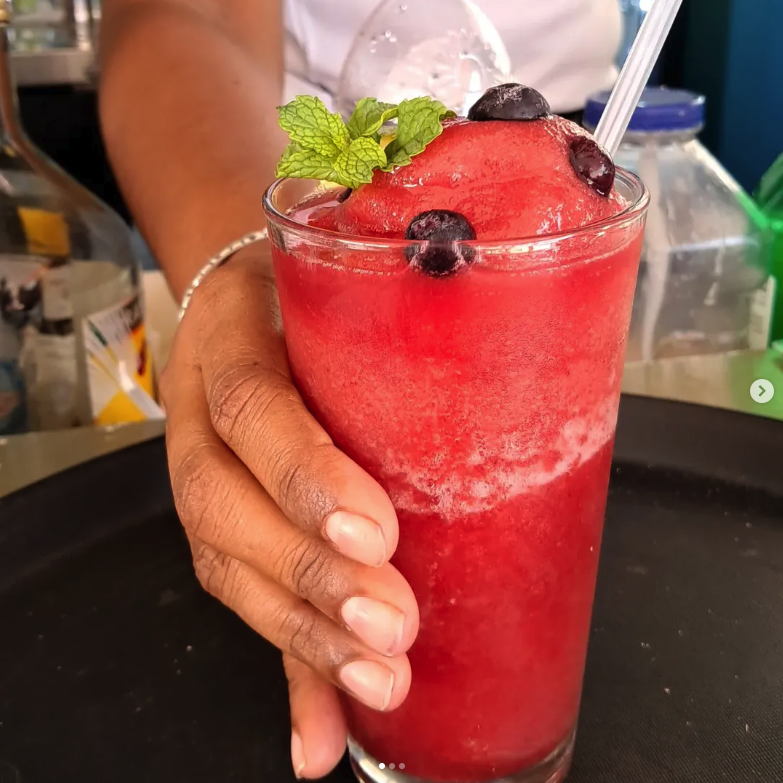 Red cocktail drink with straw, and hand holding it.